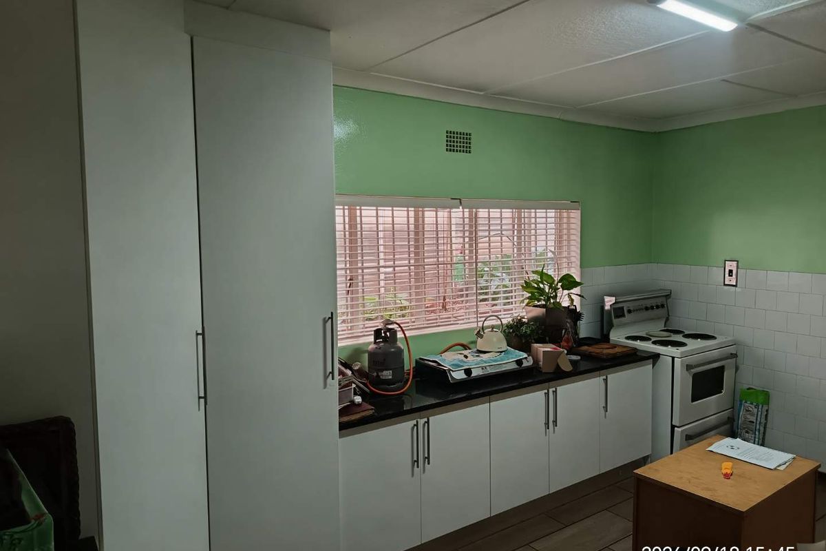 Functional kitchen featuring white cabinetry, granite countertops, a tiled backsplash, and a freestanding stove, with green painted walls and tiled flooring.