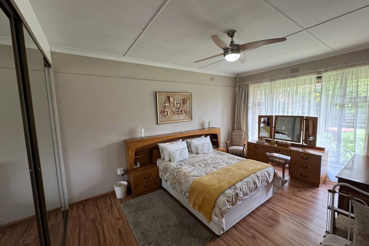 Spacious bedroom featuring laminate flooring, a ceiling fan, and built-in cupboards with sliding doors, offering direct access to the garden area.