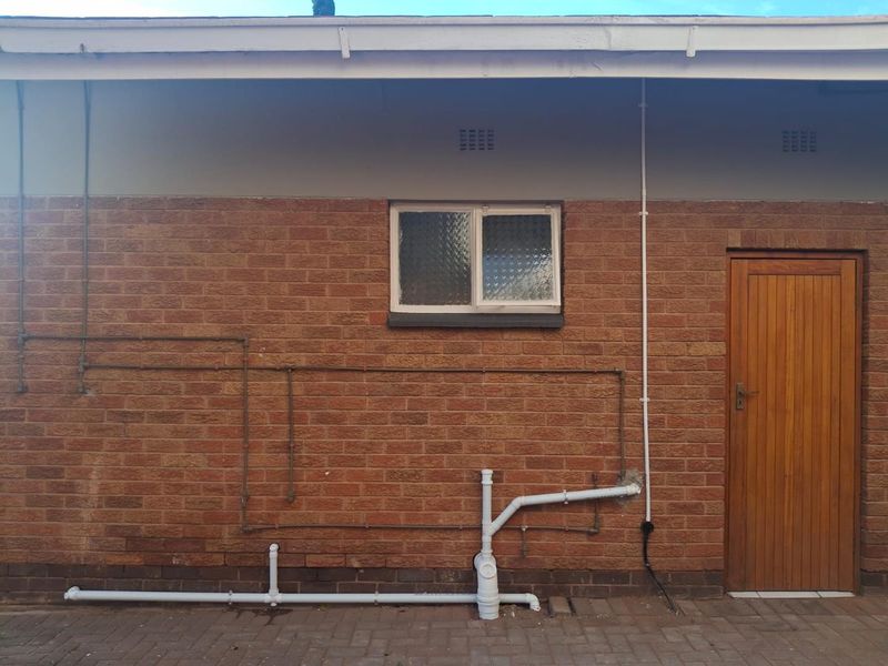 Rear exterior view of the apartment featuring exposed brickwork, a timber door, and external plumbing infrastructure.