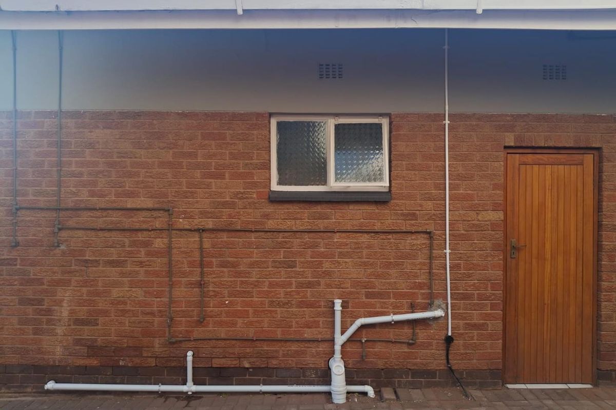 Rear exterior view of the apartment featuring exposed brickwork, a timber door, and external plumbing infrastructure.