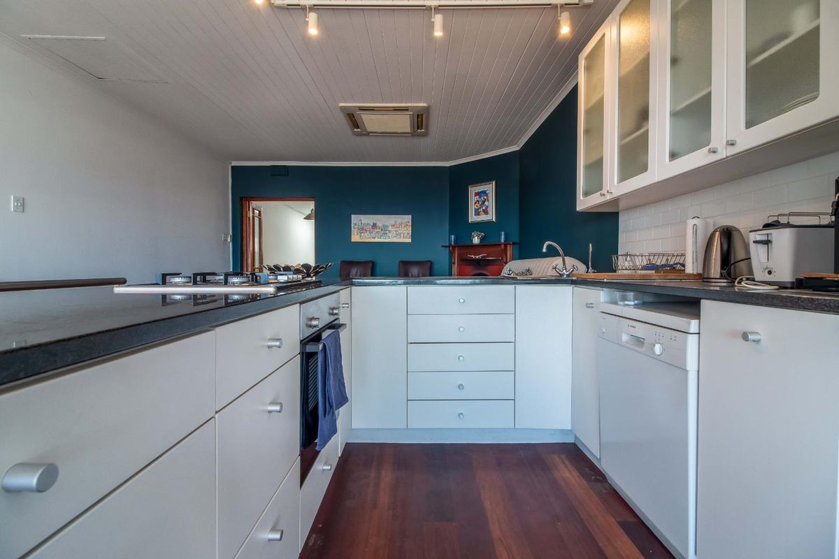 Functional kitchen featuring white cabinetry, dark countertops, integrated gas hob, oven, and dishwasher, set against a bold blue feature wall.