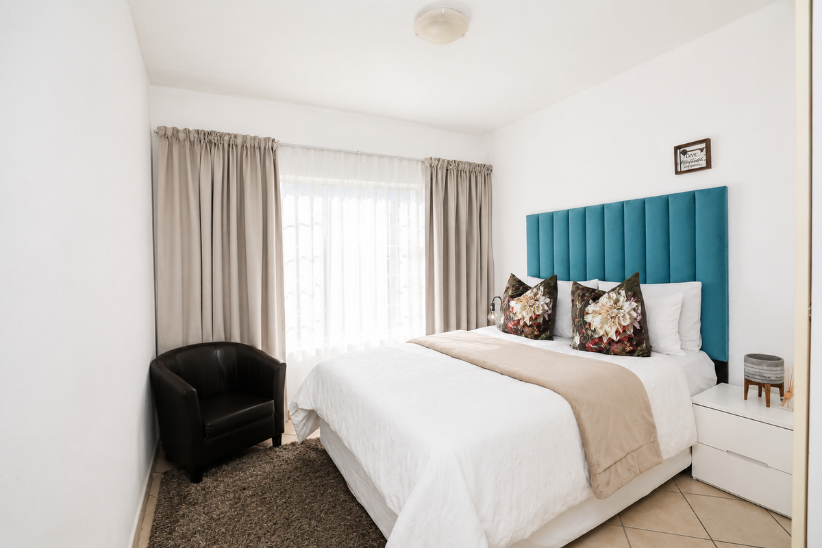 A well-maintained bedroom featuring neutral tiled flooring, a large window with curtain tracks, and a central ceiling light fixture.