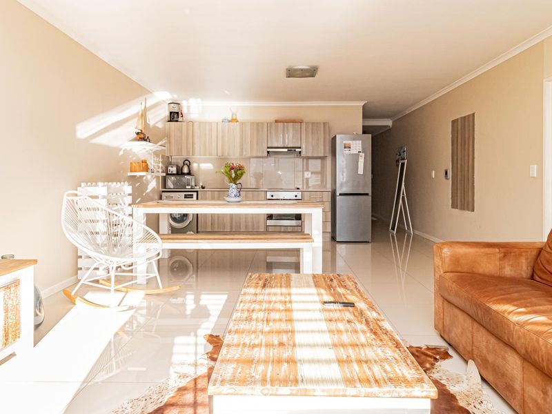 Open-plan living area featuring a modern kitchen with built-in cabinetry, oven, and hob, seamlessly flowing into a bright, tiled lounge space.