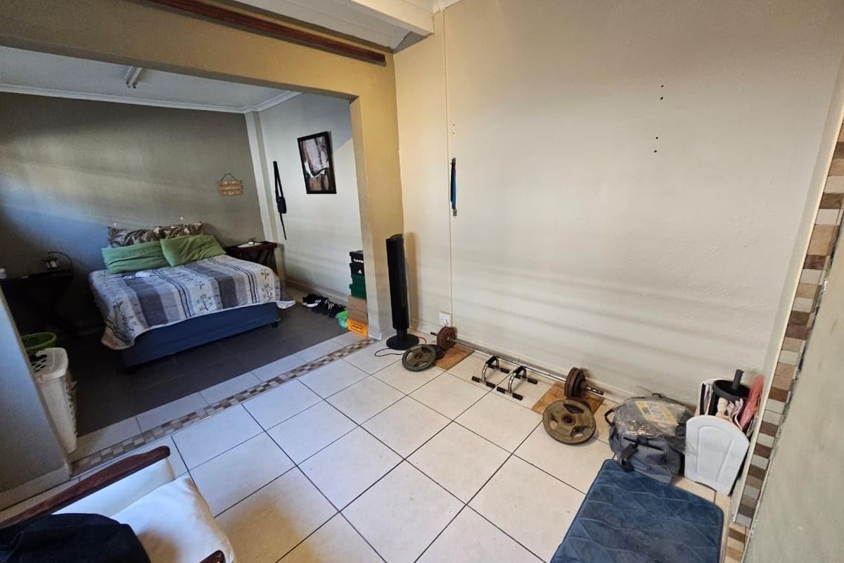 A bedroom featuring tiled flooring and a coved ceiling, with an open-plan layout connecting to an adjacent living or sleeping area.