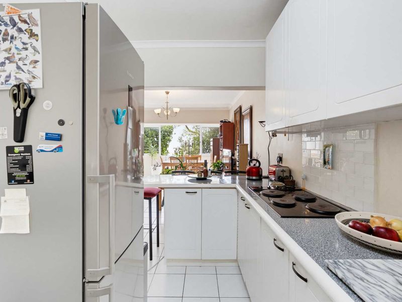 A functional kitchen featuring white cabinetry, a subway tile backsplash, and an electric hob, with an open-plan layout leading to the dining area.