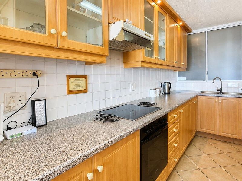 A functional kitchen featuring wooden cabinetry, laminate countertops, a built-in oven with electric hob, and tiled flooring.