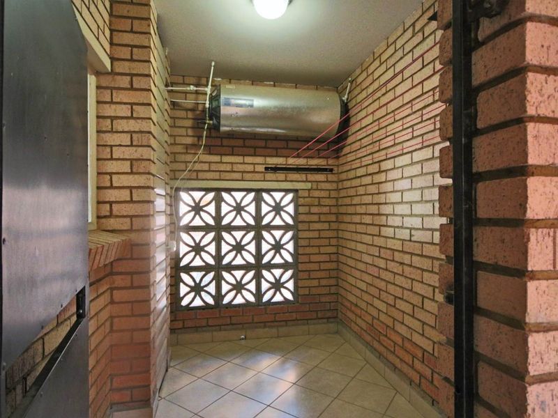 A functional laundry area featuring exposed brick walls, ceramic floor tiling, and a wall-mounted electric water heater.