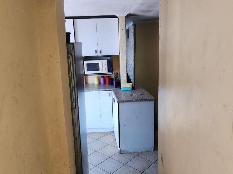 A view into a dated kitchen featuring built-in cabinetry and tiled flooring, showing signs of wear and requiring maintenance or renovation.