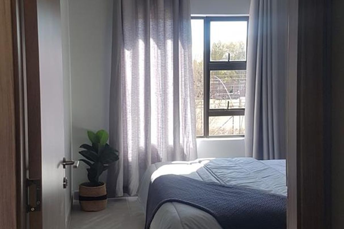 A view through a doorway into a bedroom featuring tiled flooring, neutral walls, and a window with curtains.