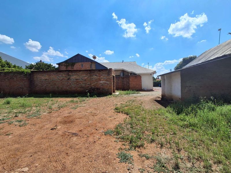Rear exterior view of the property featuring an unpaved yard, brick boundary walls, and an outbuilding with a corrugated metal roof.