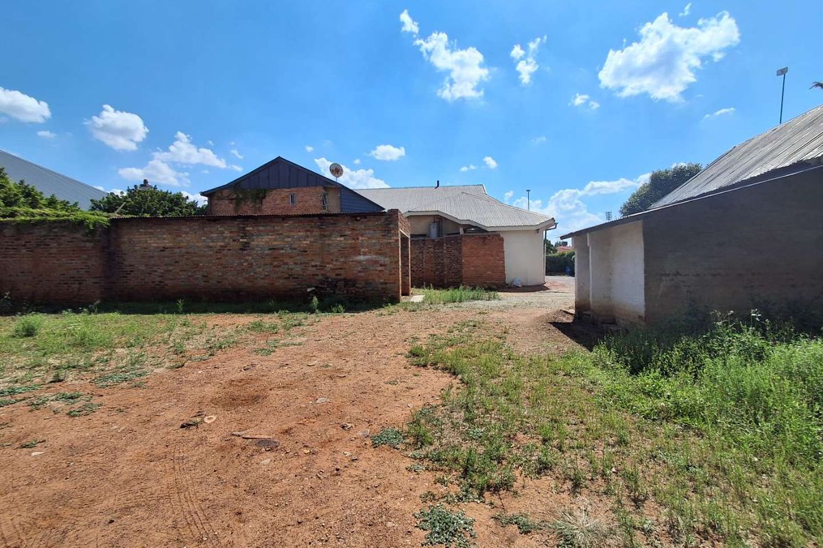 Rear exterior view of the property featuring an unpaved yard, brick boundary walls, and an outbuilding with a corrugated metal roof.