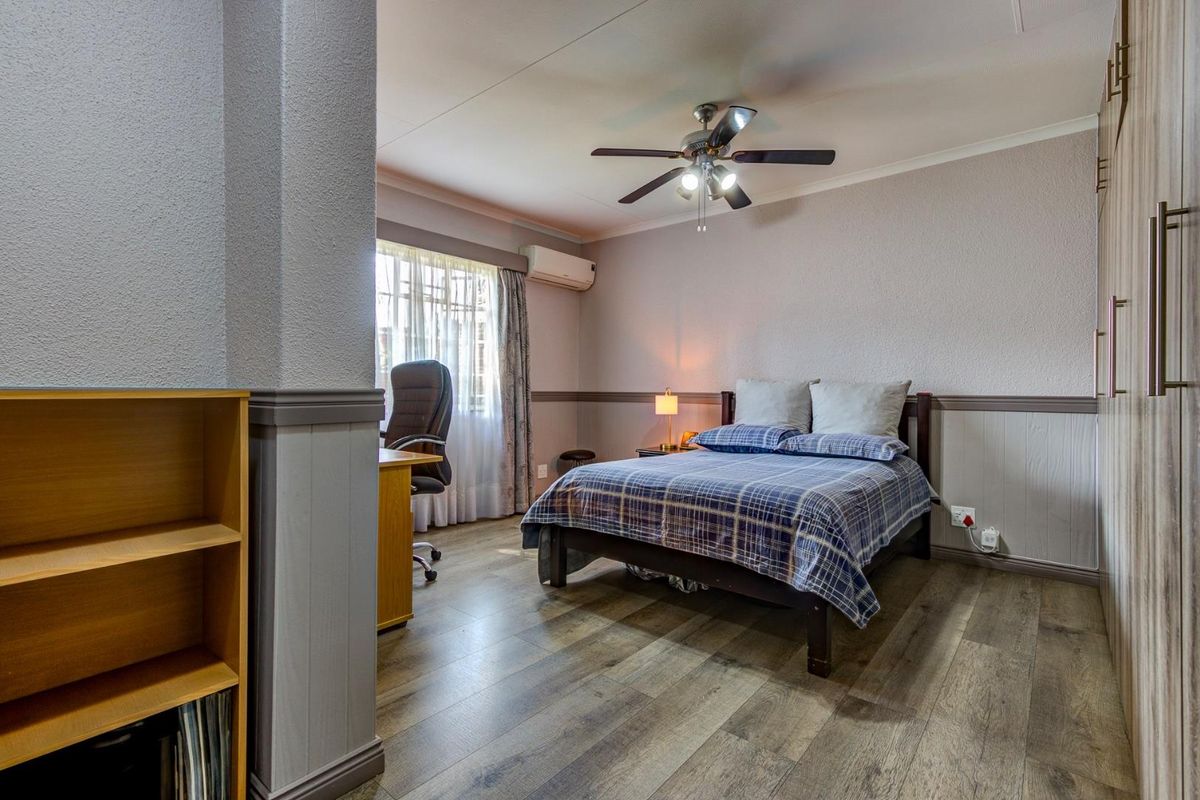 A well-maintained bedroom featuring laminate flooring, built-in cupboards, wainscoting, a ceiling fan, and a wall-mounted air conditioning unit.