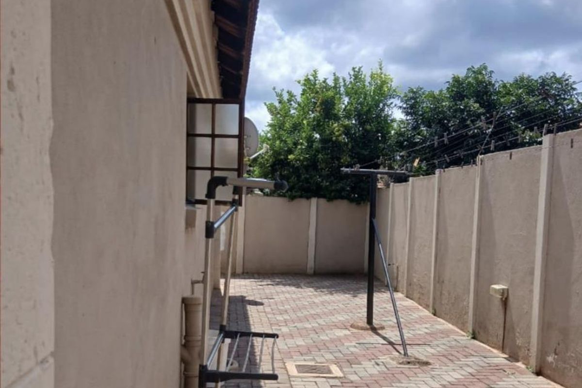 A paved side yard area featuring a high boundary wall with security fencing and a tiled roof overhang.