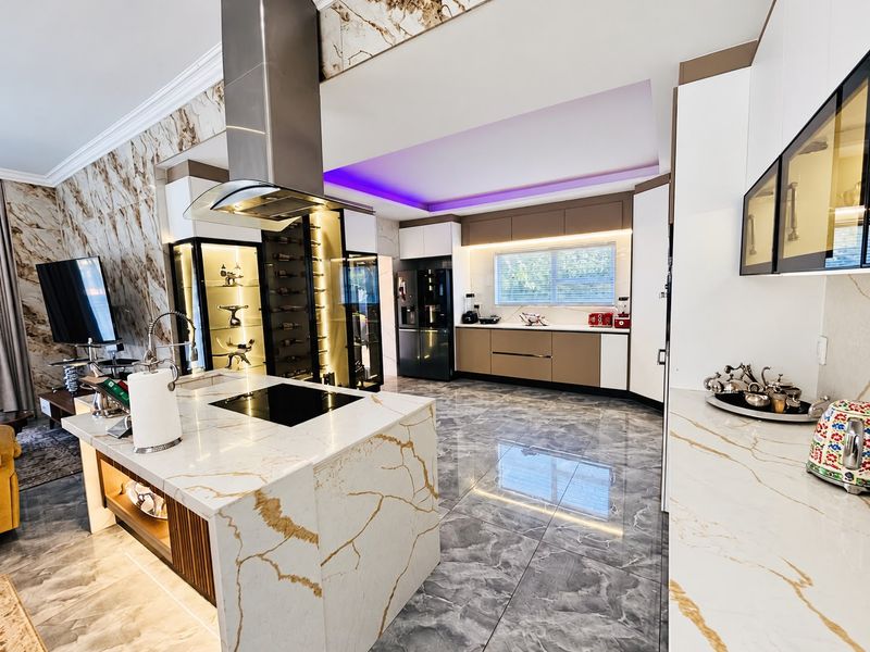 Modern luxury kitchen featuring a marble-look island with integrated cooktop, high-end cabinetry, built-in wine storage, and premium porcelain flooring with ambient LED lighting.