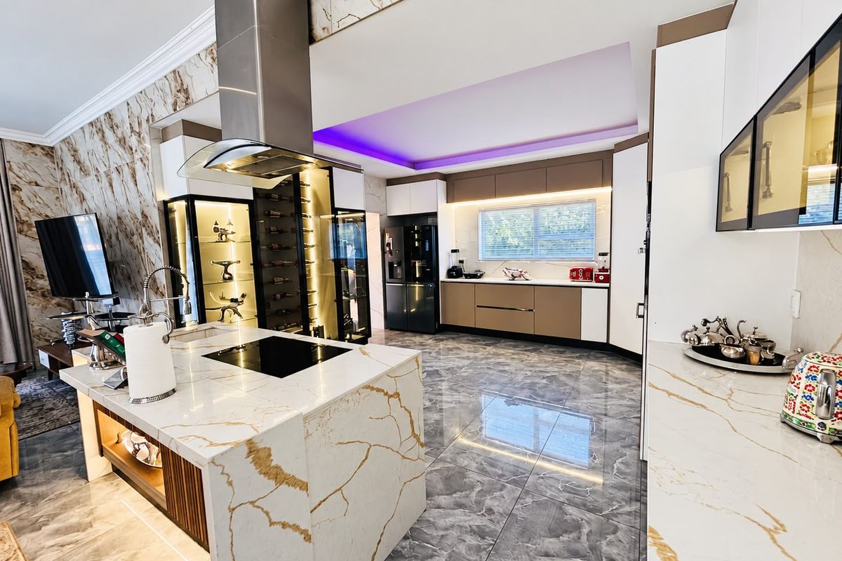 Modern luxury kitchen featuring a marble-look island with integrated cooktop, high-end cabinetry, built-in wine storage, and premium porcelain flooring with ambient LED lighting.