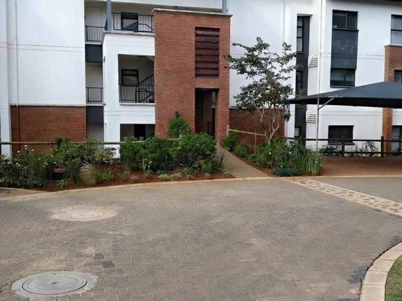Front exterior view of an apartment complex featuring a paved driveway, brick facade detailing, and covered parking areas.