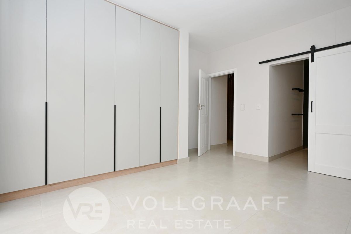 A bright, modern bedroom featuring extensive built-in cupboards, neutral tiled flooring, and a stylish sliding barn door leading to an adjacent space.