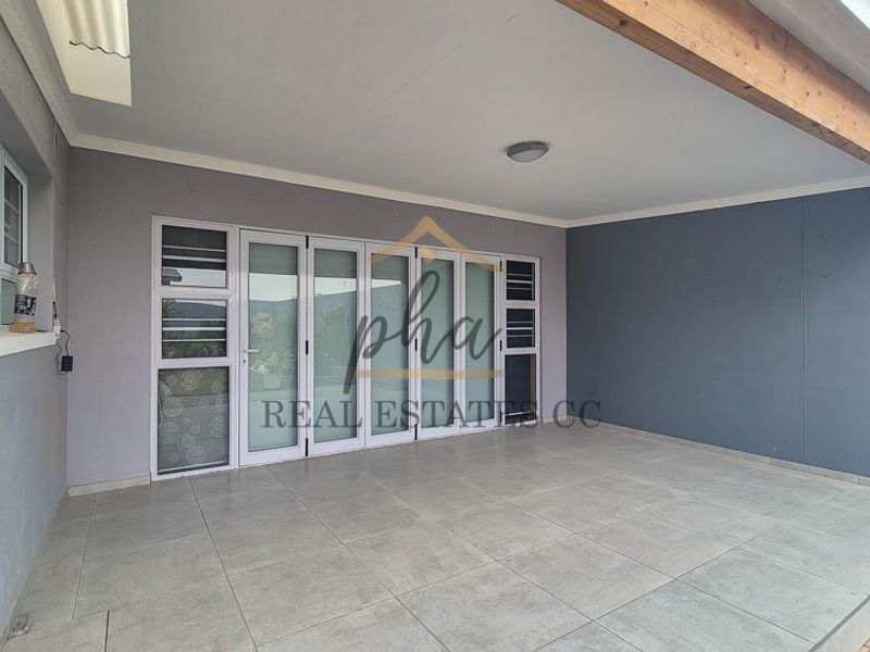 A spacious covered patio featuring large format floor tiles, an exposed timber beam, and modern bi-fold glass doors providing access to the interior.