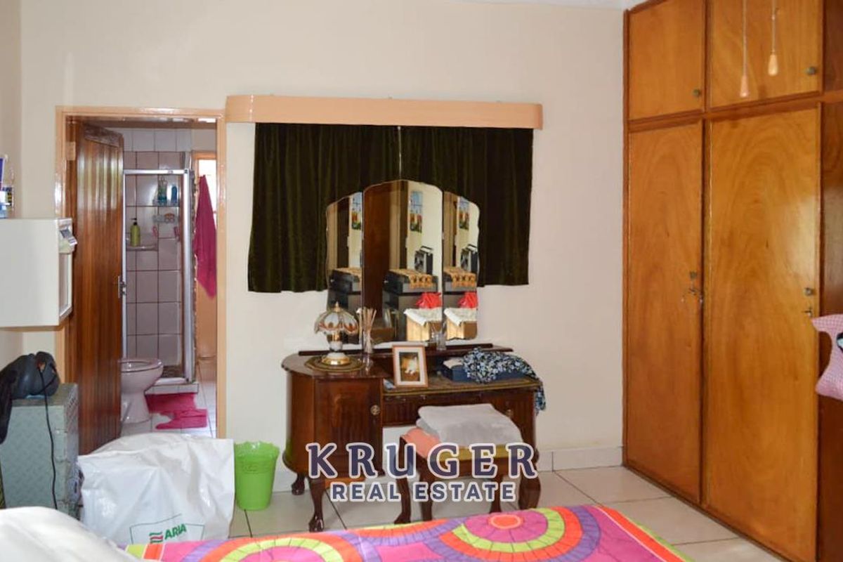 A bedroom featuring built-in wooden cupboards and an en-suite bathroom with tiled flooring.