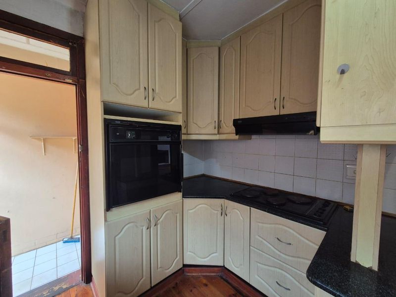 A dated kitchen featuring built-in cabinetry, an integrated oven, electric hob, and extractor fan, with timber flooring and tiled backsplash.