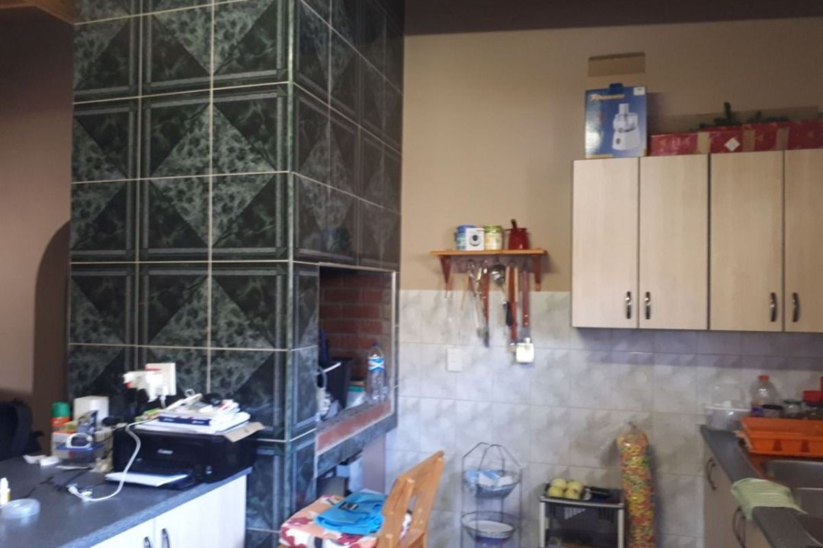 A kitchen area featuring a built-in indoor braai or fireplace with dark decorative tiling, light-toned cabinetry, and tiled splashbacks.