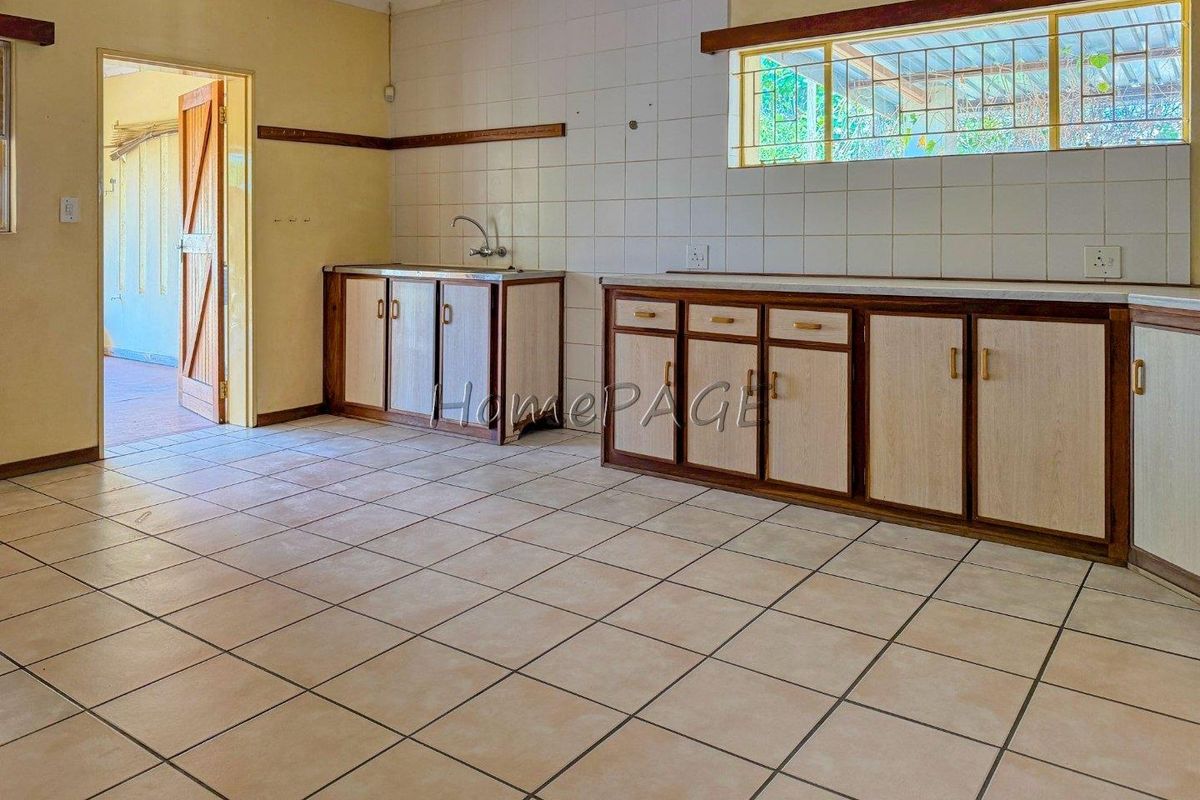 A spacious, empty kitchen featuring tiled flooring, built-in cabinetry, and a stainless steel sink, offering a blank canvas for renovation.
