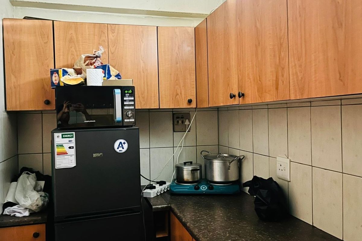 A compact kitchen featuring wood-look laminate cabinetry, dark countertops, and tiled splashbacks, providing functional storage and preparation space.