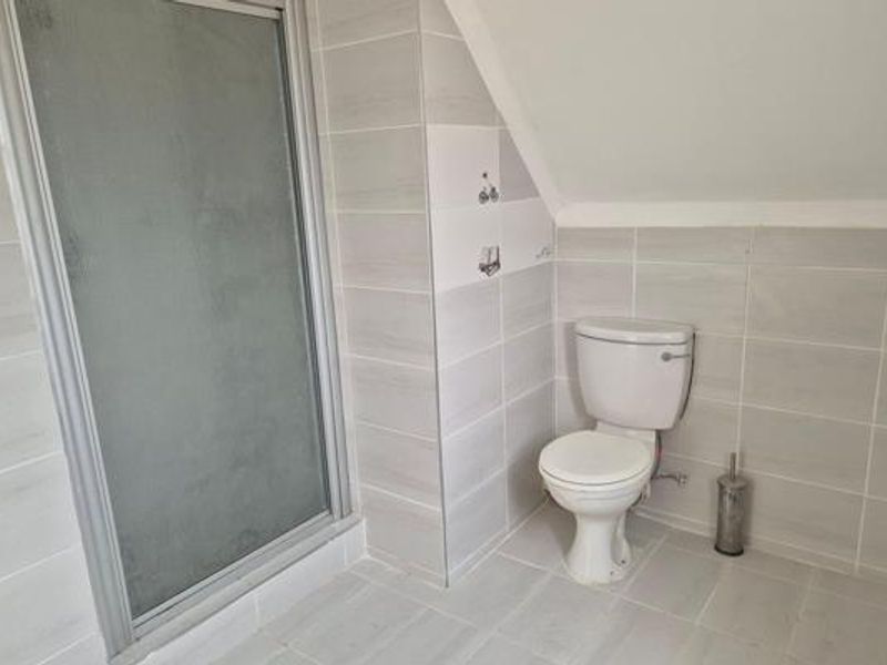 A clean, modern bathroom featuring a glass-enclosed shower and a standard toilet with neutral grey wall and floor tiling.