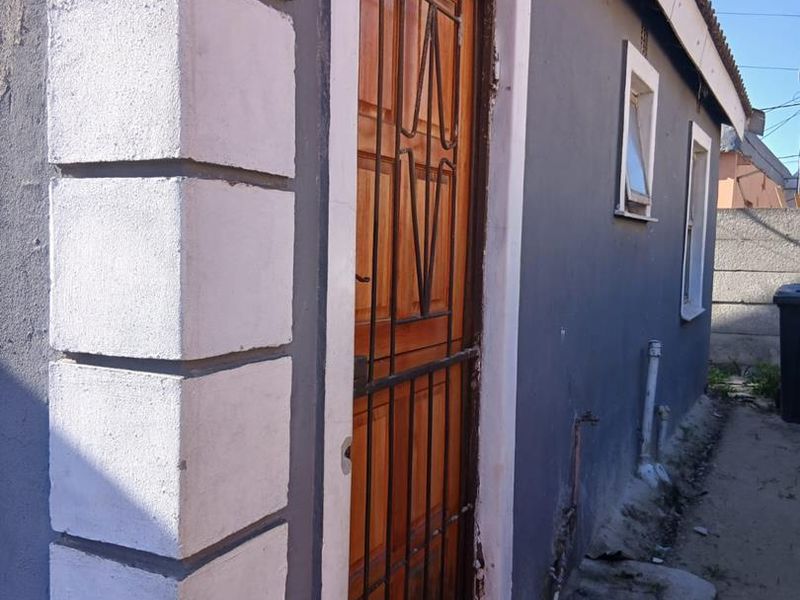 Side view of the property showing a timber door with security gate, external plumbing fixtures, and painted masonry walls.
