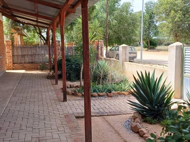 A covered outdoor patio area featuring brick paving, timber support beams, and a view of the garden and perimeter fencing.