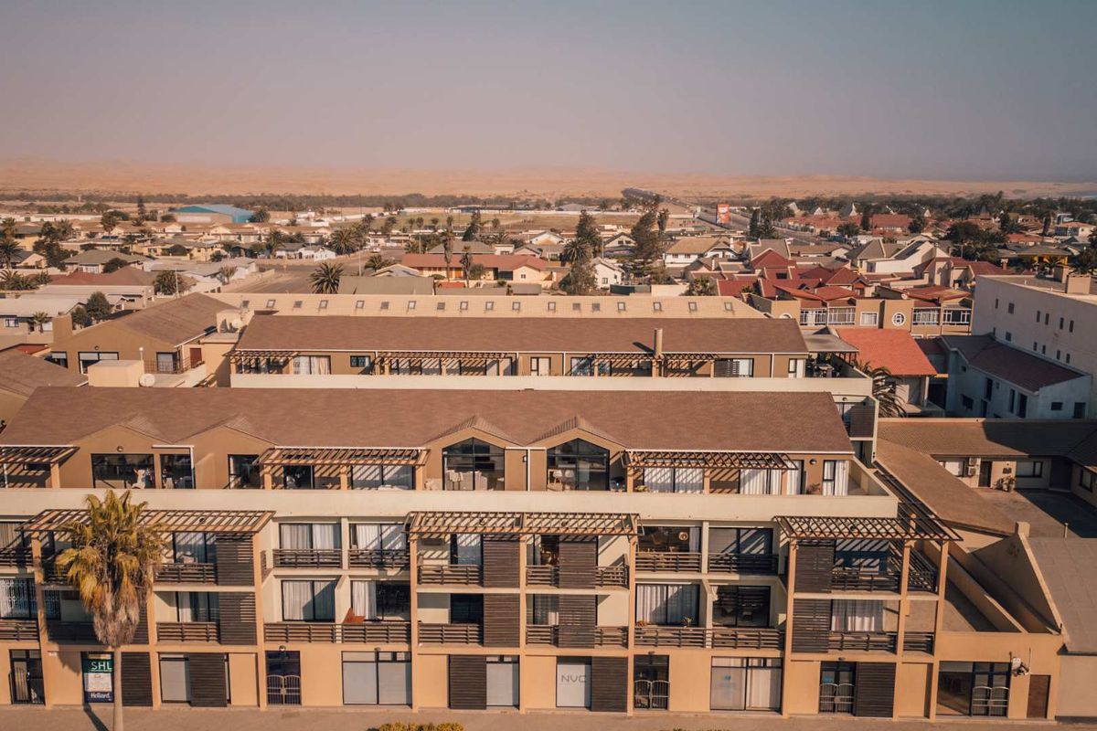 Aerial view of a multi-story apartment complex featuring balconies with timber pergolas and a surrounding coastal residential neighborhood.