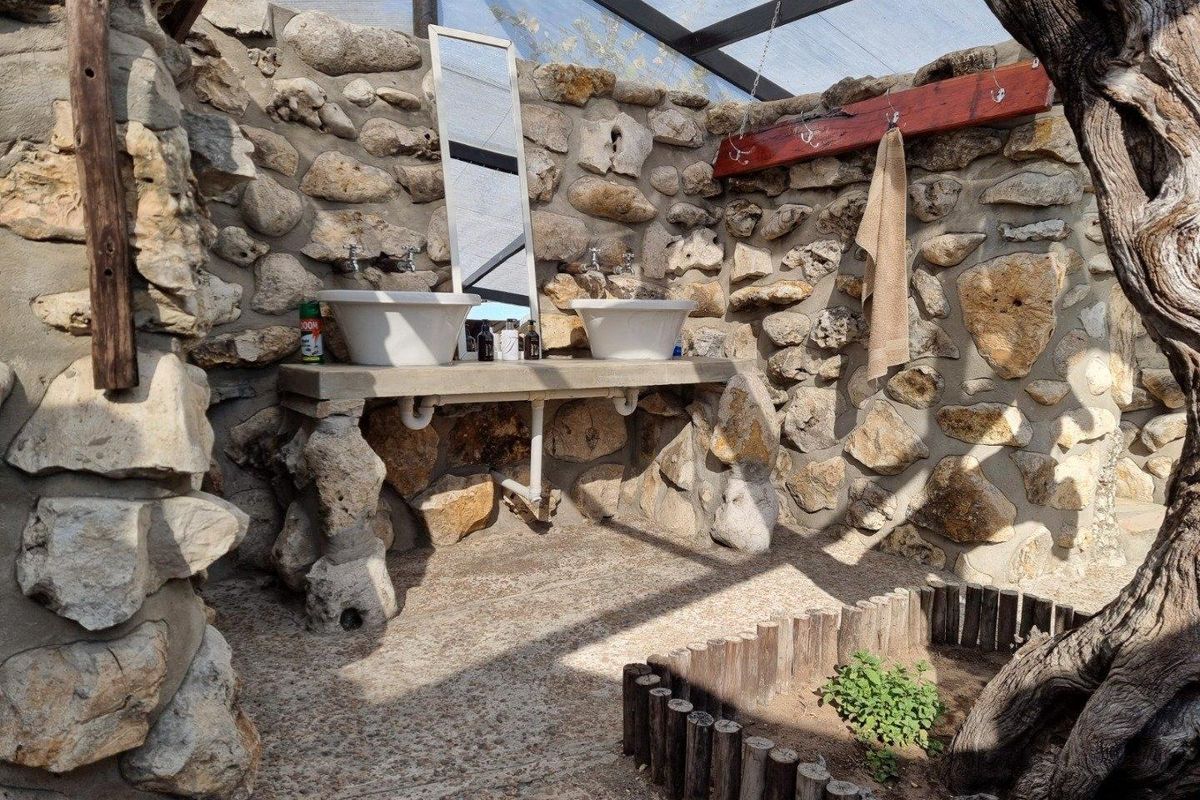 Rustic outdoor bathroom area featuring dual vessel sinks set on a stone vanity against a natural stone wall under a covered structure.