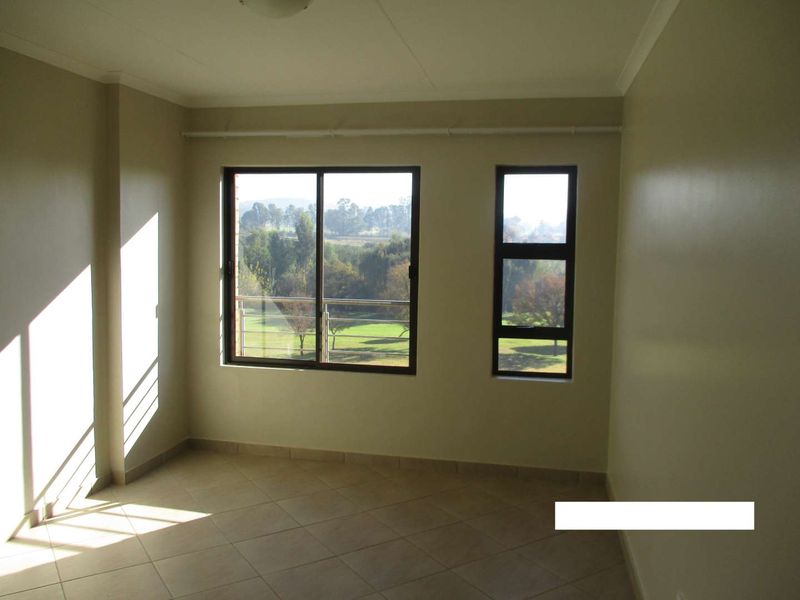 A bright, empty bedroom featuring neutral tiled flooring and large aluminium-framed windows with views of the surrounding landscape.