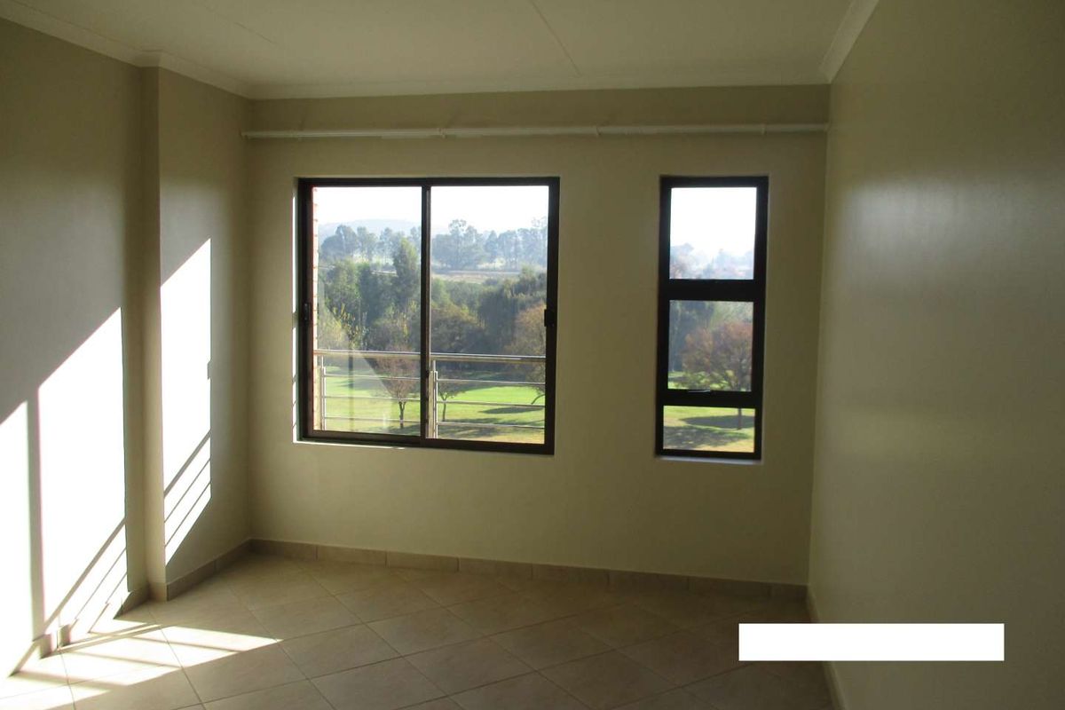 A bright, empty bedroom featuring neutral tiled flooring and large aluminium-framed windows with views of the surrounding landscape.