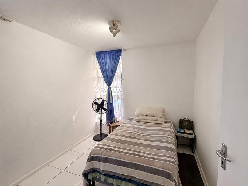 A compact bedroom featuring tiled flooring, a security gate on the window, and a ceiling-mounted spotlight fixture.