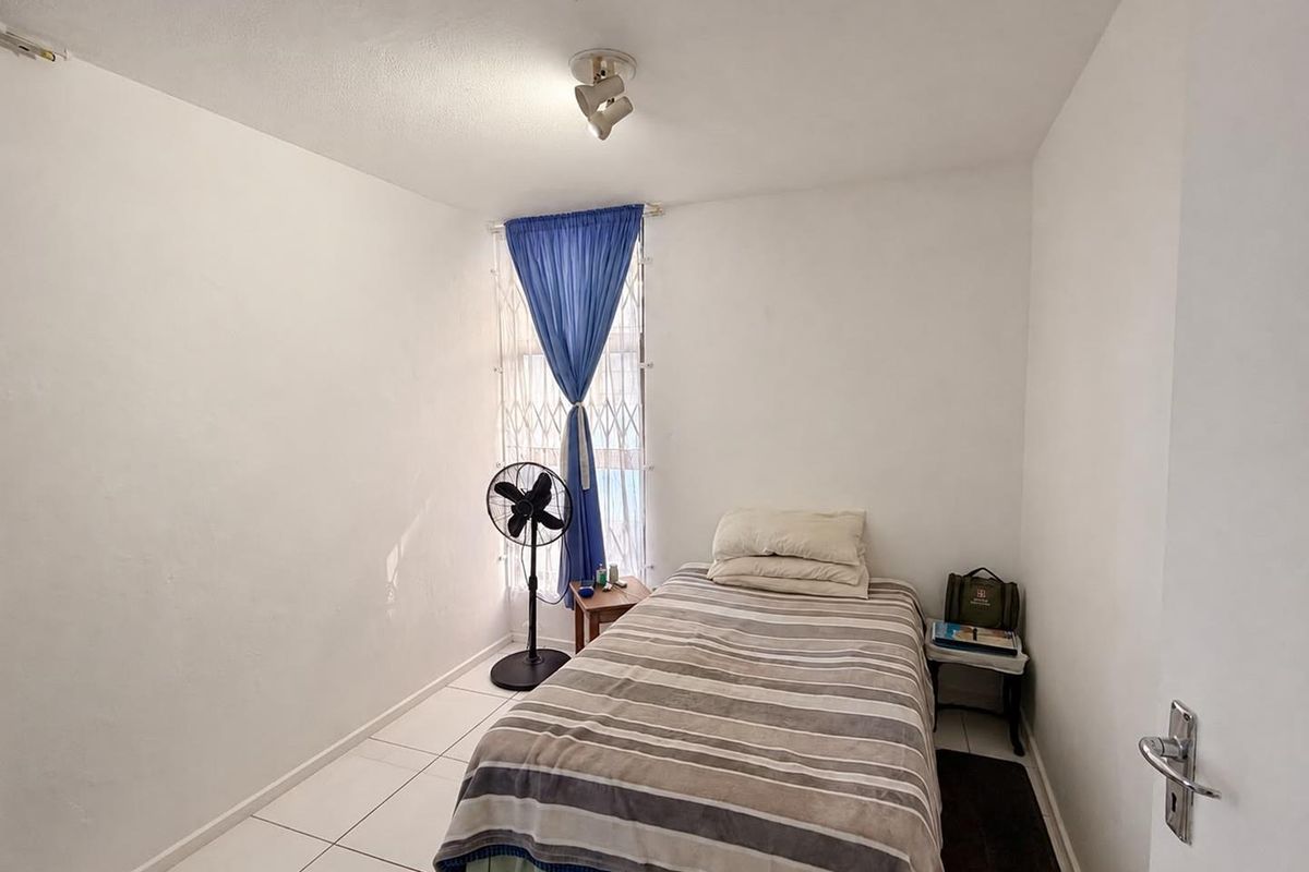 A compact bedroom featuring tiled flooring, a security gate on the window, and a ceiling-mounted spotlight fixture.