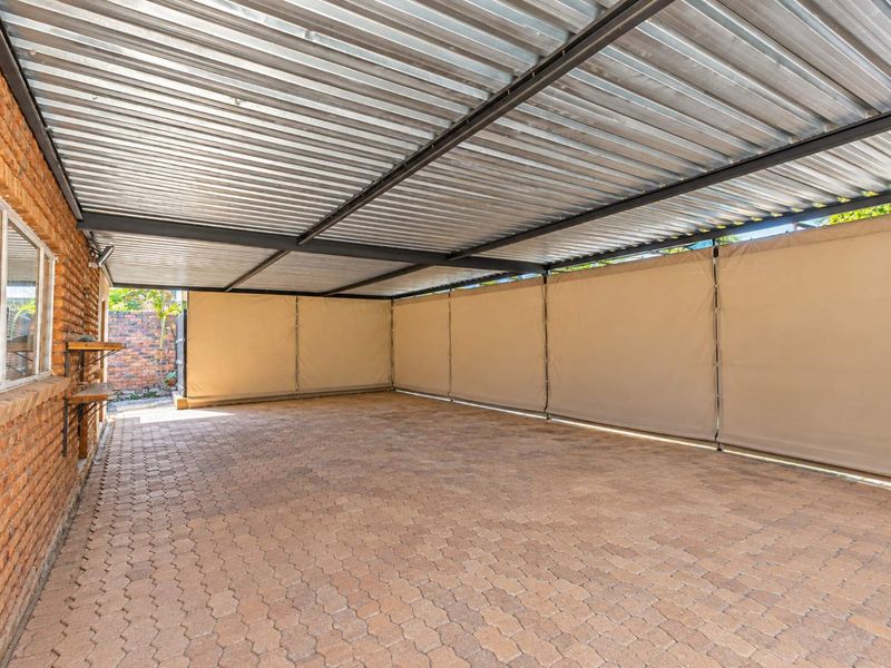 A spacious covered patio area featuring durable paved flooring, a corrugated metal roof, and retractable canvas side screens for versatile outdoor living.