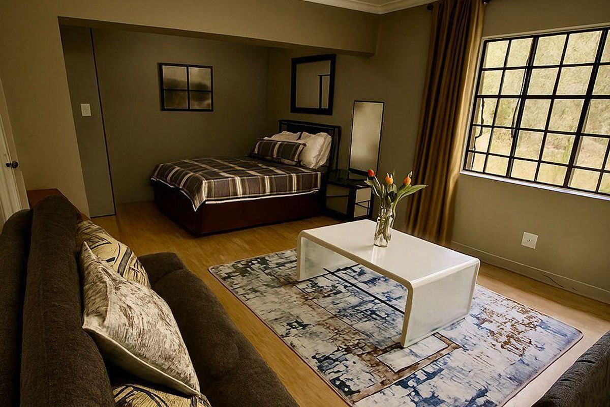 A spacious bedroom featuring laminate flooring, a large grid-pattern window, and neutral wall tones, offering a comfortable and well-maintained living space.