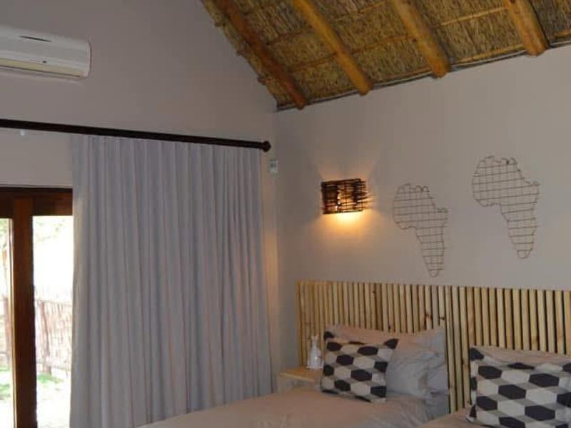 A well-maintained bedroom featuring a high vaulted thatched ceiling with exposed timber rafters, a modern chandelier, and direct access to the outdoors.