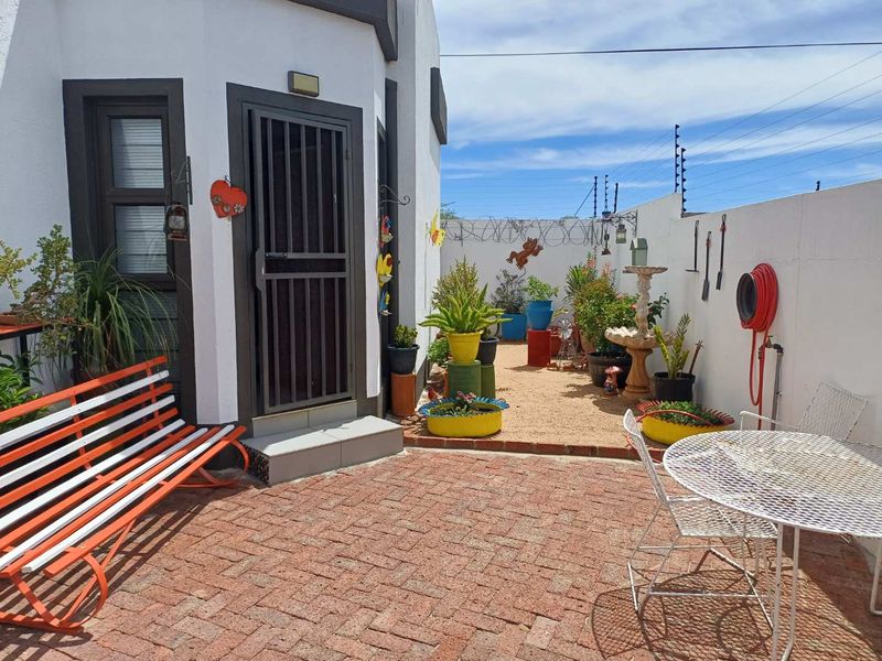 A paved outdoor patio area featuring a secure entrance, perimeter wall with electric fencing, and an outdoor water connection.