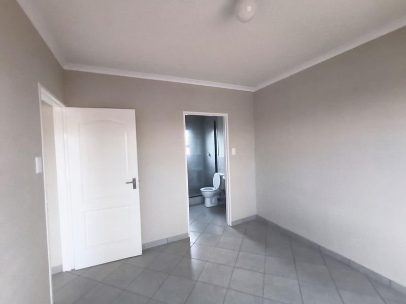 A clean, empty bedroom featuring neutral wall tones, tiled flooring, and direct access to an en-suite bathroom.