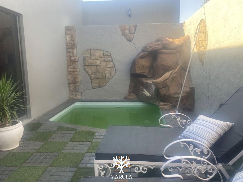 Small plunge pool area featuring a decorative rock wall and paved patio with artificial grass accents, requiring maintenance to the pool water and wall finish.