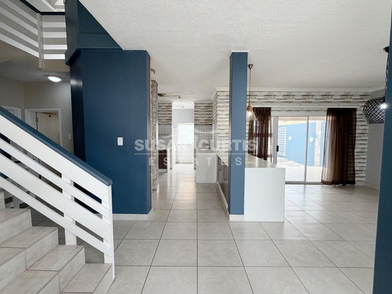 Spacious open-plan living area featuring tiled flooring, a central kitchen island, and a staircase, with direct access to the outdoor patio area.