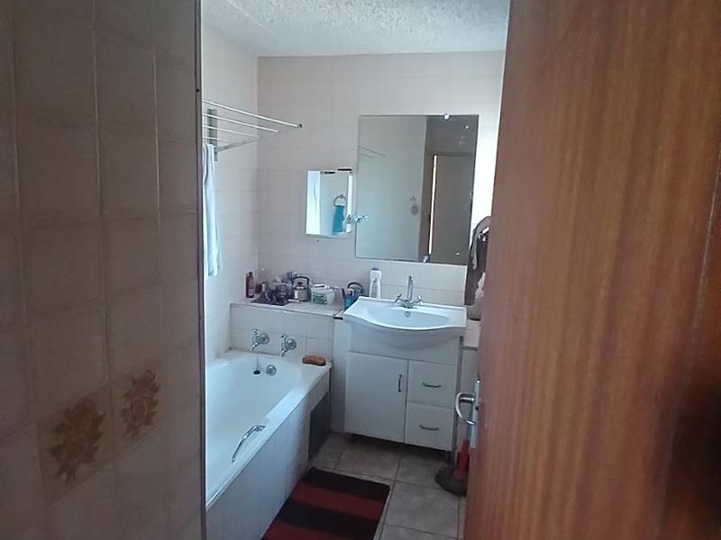 A dated bathroom featuring a bathtub, vanity cabinet with integrated basin, and tiled finishes. The space would benefit from modern updates and cosmetic improvements.