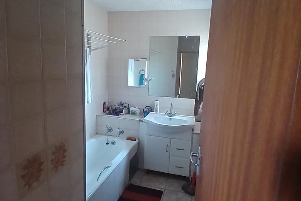 A dated bathroom featuring a bathtub, vanity cabinet with integrated basin, and tiled finishes. The space would benefit from modern updates and cosmetic improvements.