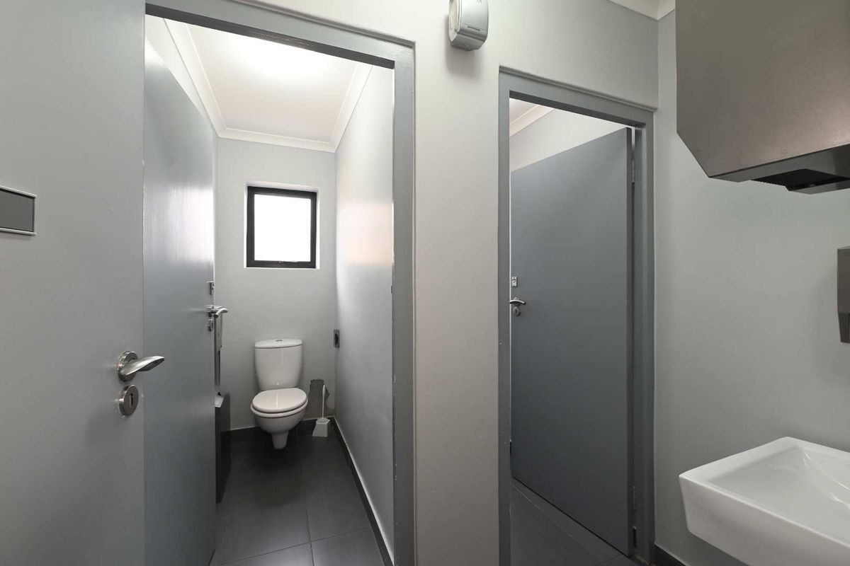 A clean, modern bathroom area featuring a toilet, wall-mounted basin, and neutral grey tones with tiled flooring.