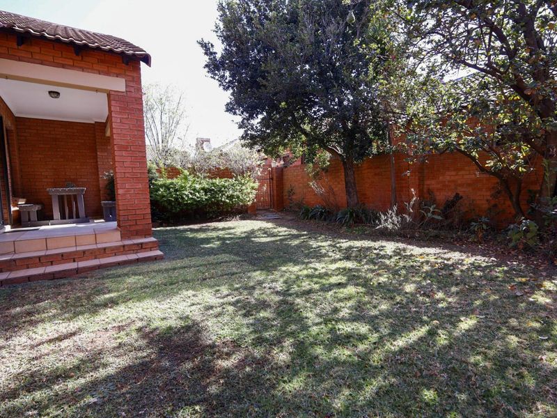 A private rear garden featuring a covered brick patio, established trees, and a secure brick boundary wall.
