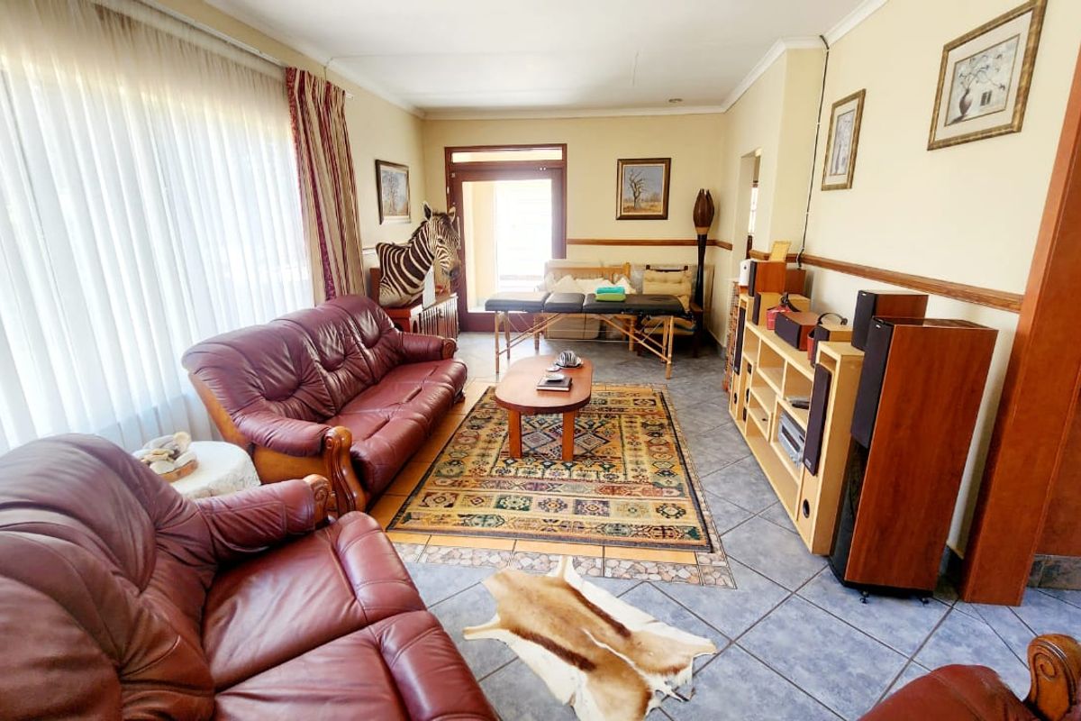 A spacious living room featuring tiled flooring, a chair rail, and large windows that provide ample natural light, with access to an outdoor area.