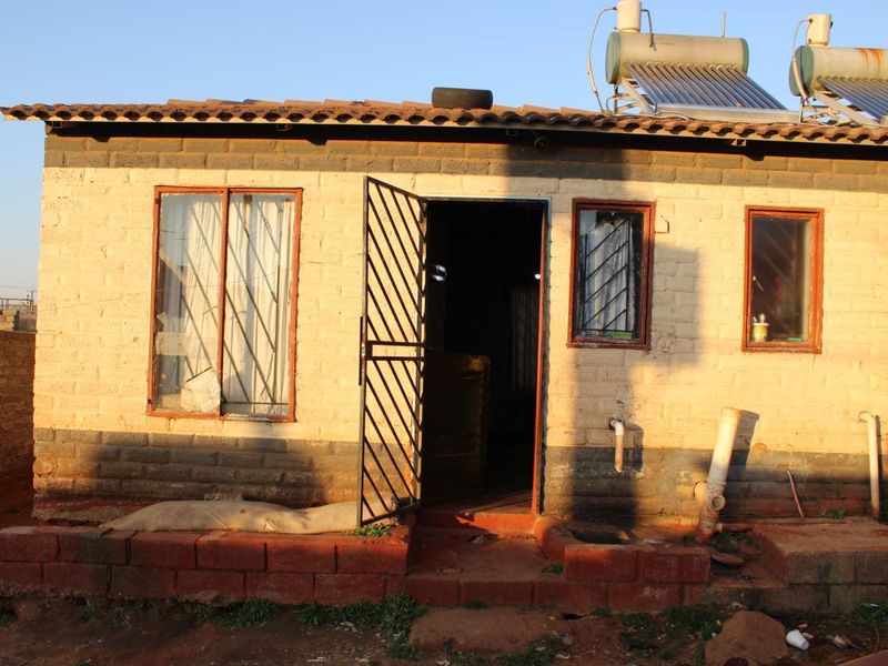 Front elevation of a single-story brick house featuring a solar water heating system, security gate, and metal-framed windows.