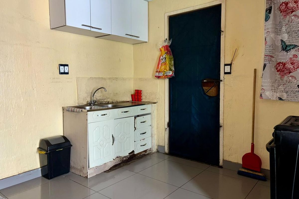 A compact kitchen area featuring basic cabinetry, a stainless steel sink, and tiled flooring, currently requiring maintenance and cosmetic updates.